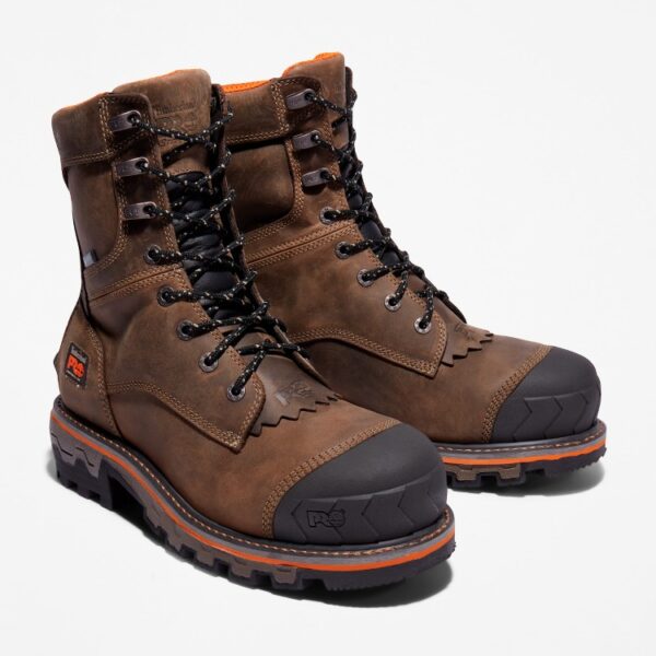 A turned pair of Timberland Boondock HD composite toe men's logger work boots in brown with a blank background.