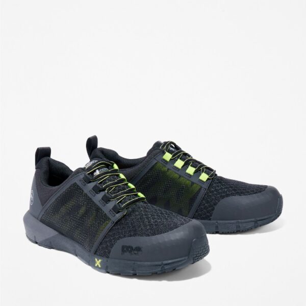 A turned pair of Timberland Radius composite toe low top men's work sneakers in black and green with a blank background.