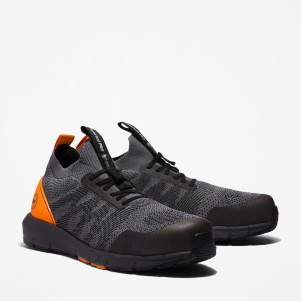 A turned pair of Timberland Radius composite toe men's work sneakers in gray and orange with a blank background.