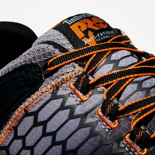 Close up of Timberland PRO Powertrain Sport alloy toe men's work sneakers in orange and black showing anti-fatigue technology tag with a blank background.