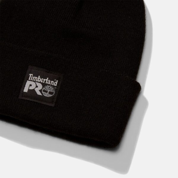 A close up look at the Timberland Watch Cap in black with a focus on the Timberland PRO tag on a blank background.