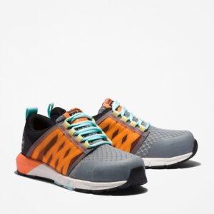 A turned pair of Timberland Radius composite toe women's work sneakers in gray, orange, black and light blue with a blank background.