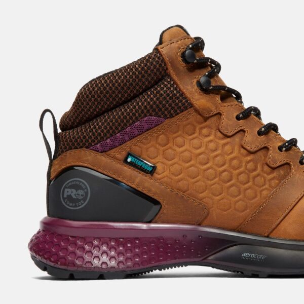 Close up of Timberland Reaxion safety toe women's work sneaker in tan and purple showing composite toe stamp and waterproof tag with a blank background.