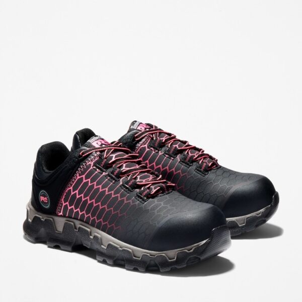 A turned pair of Timberland PRO Powertrain Sport alloy toe women's work sneakers in black and pink with a blank background.