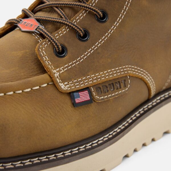 A closeup image of the left boot on a Brunt USA Marin Welted Unlined Limited Edition soft toe men's 6-inch work boot in dark tan showing brand patch, logo lace tag, and US flag tag with a blank background.